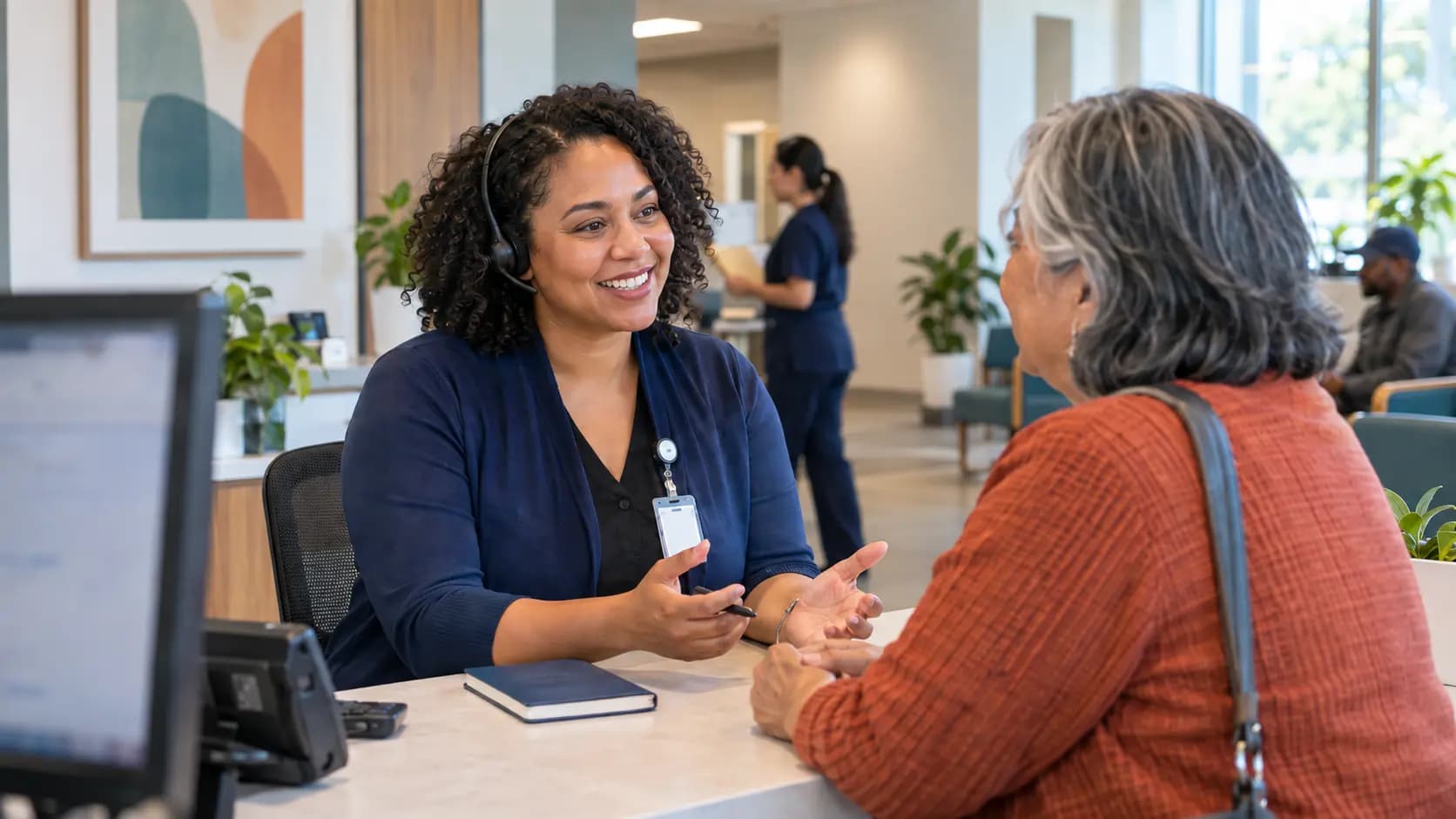 Reception colleague wearing a headset and talking with a visitor across a clinic desk