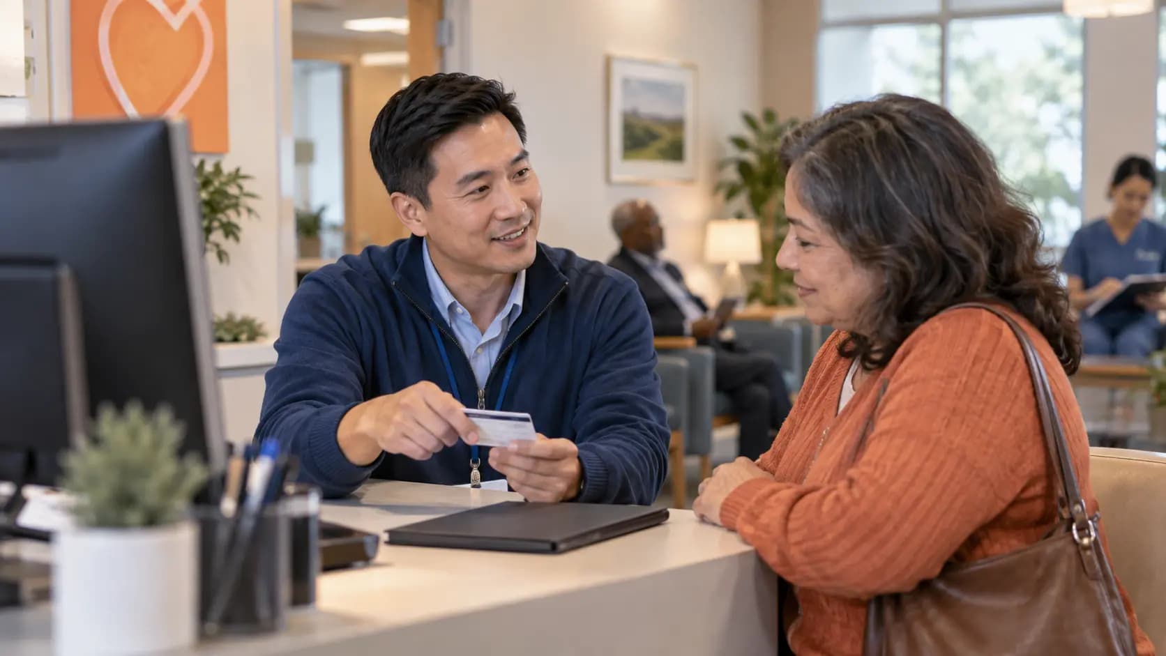 Patient-access coordinator helping a patient at a clinic desk Patient-access coordinator helping a patient at a clinic desk