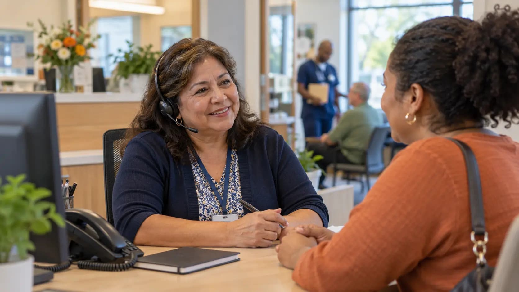 Reception colleague wearing a headset and speaking with a visitor across a clinic desk
