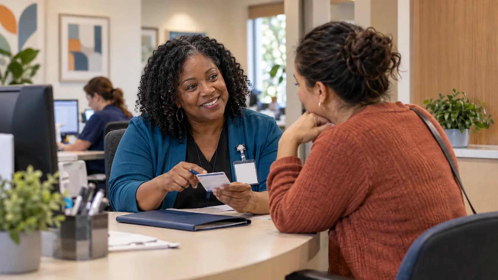 Patient-access coordinator helping a patient at a clinic desk Patient-access coordinator helping a patient at a clinic desk